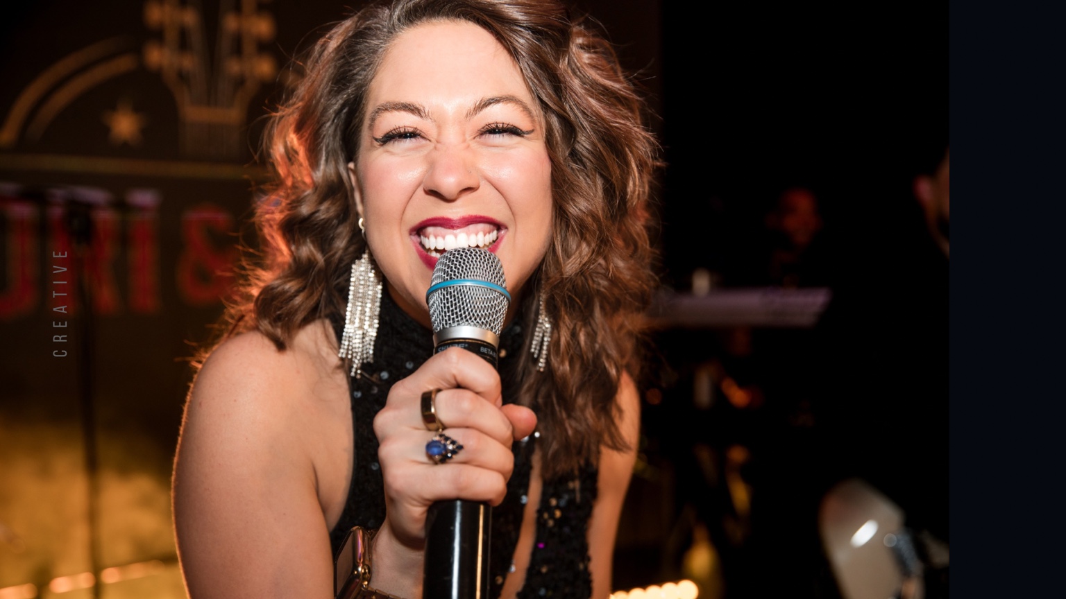 Tori smiling into the microphone under warm gold stage lights